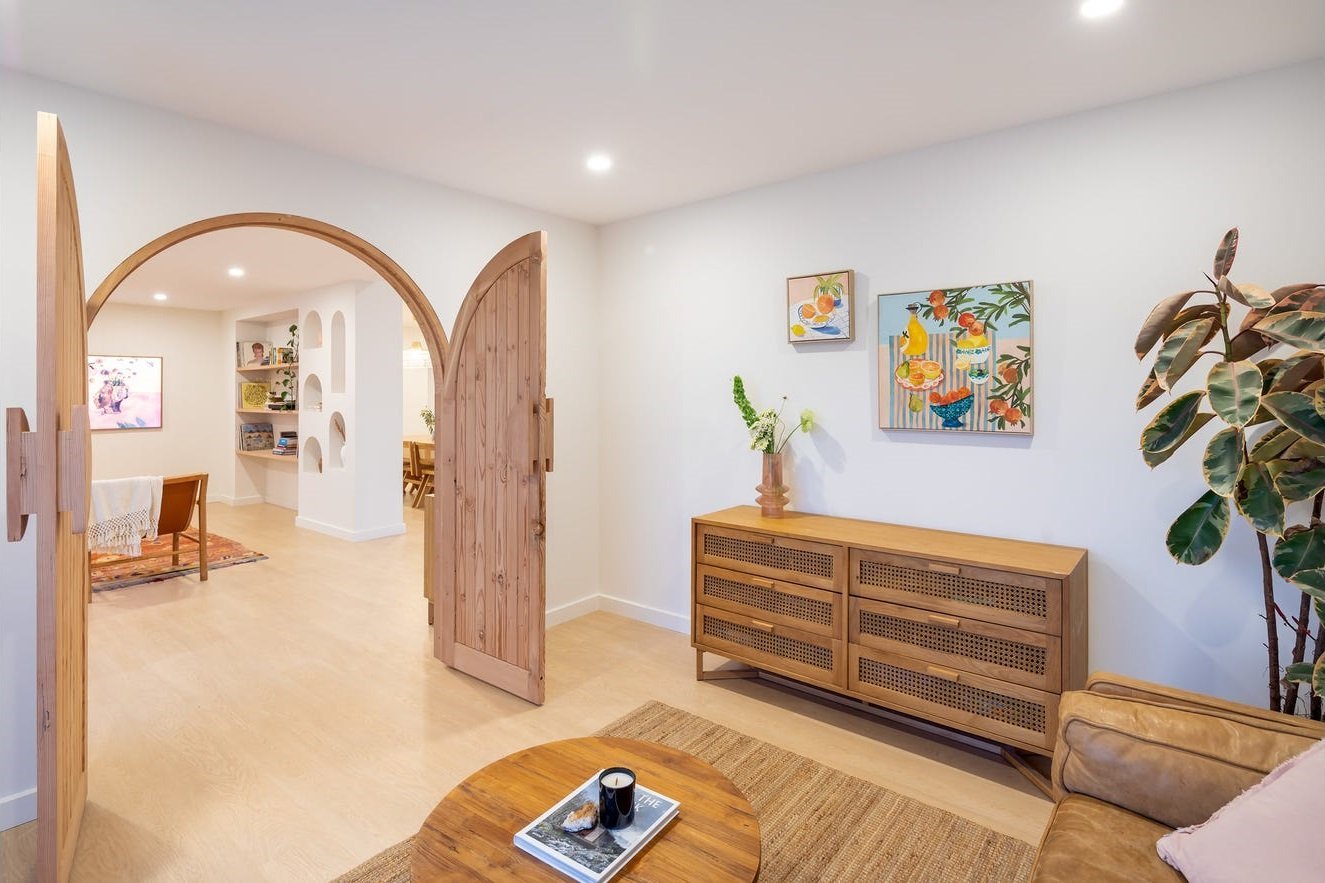Arched solid-timber door opening into a bright living room with a matching archway