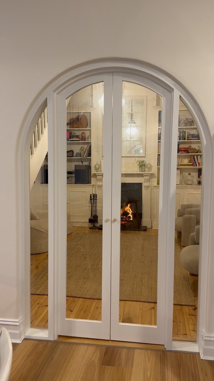 Arched white-painted internal double doors opening into a living room with fireplace