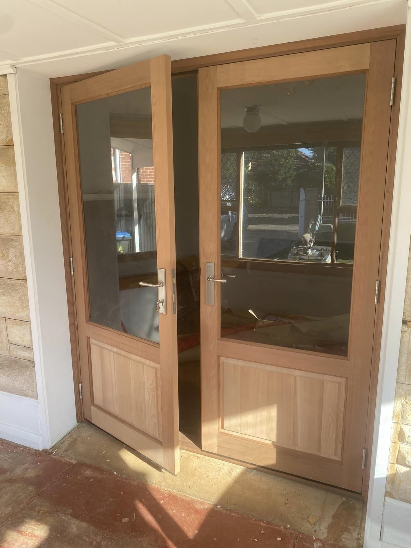 Timber double entry doors with glazed panels, one door open showing the deadbolt hardware