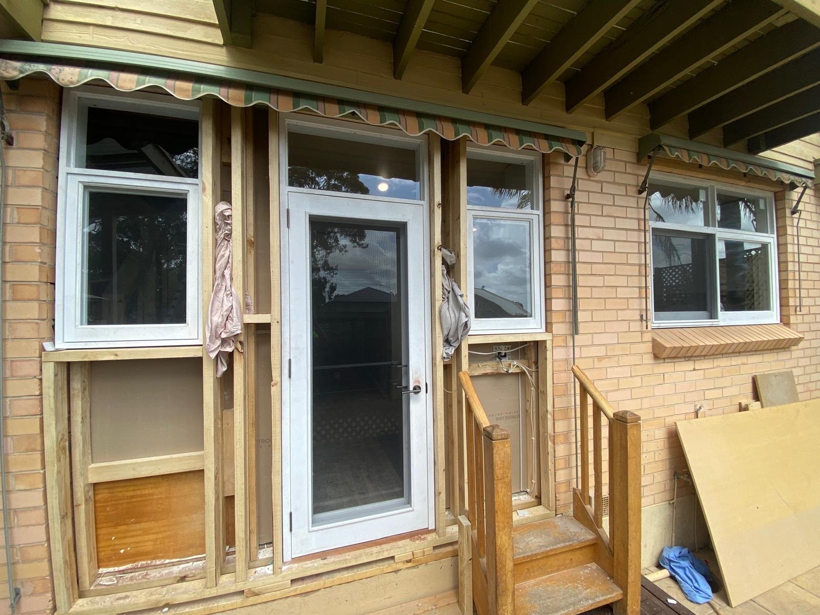 White French door with flanking awning windows, installed on a brick home renovation
