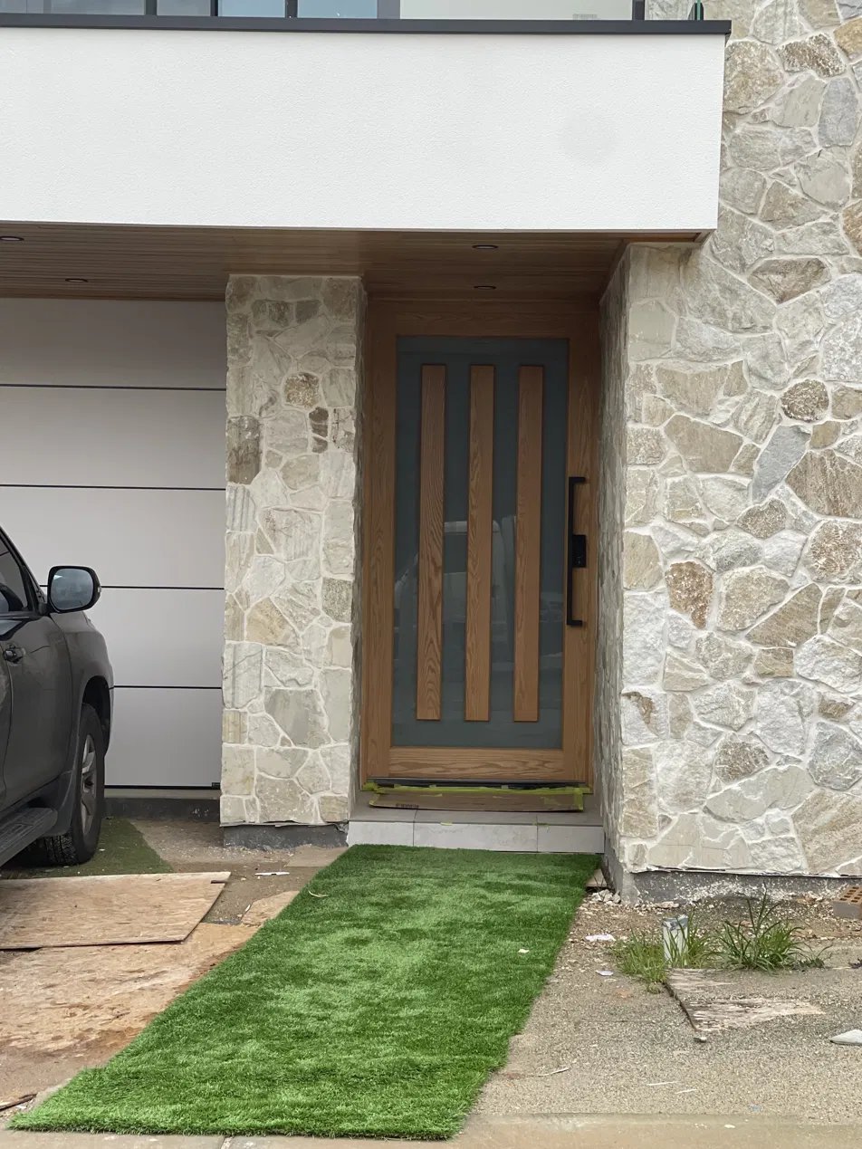 Modern entry door with vertical timber slat detailing set in a stone-clad entryway