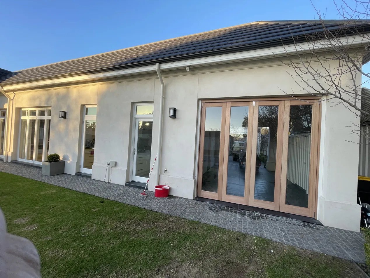Four-panel timber bifold door opening onto a paved courtyard on a rendered home