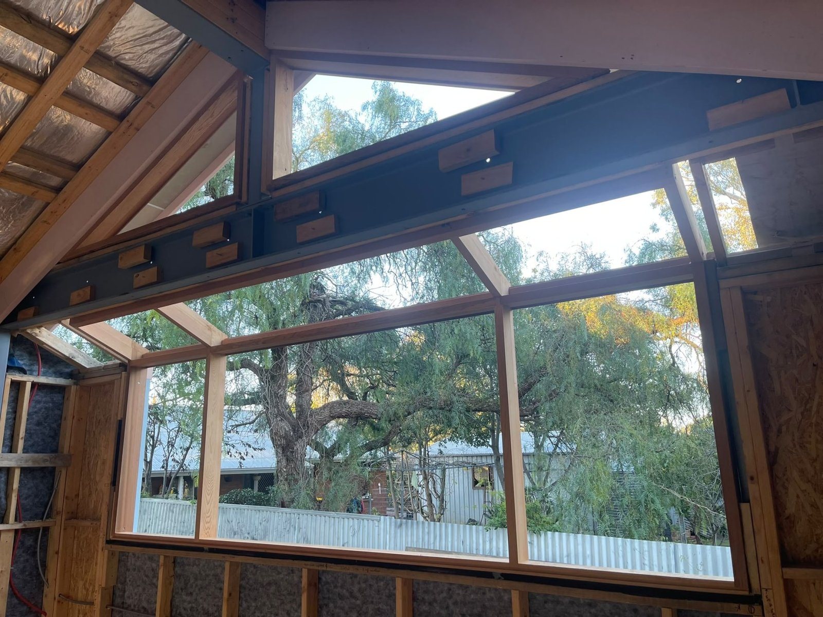 Large raked-gable timber-framed window wall under construction, cathedral ceiling glazing