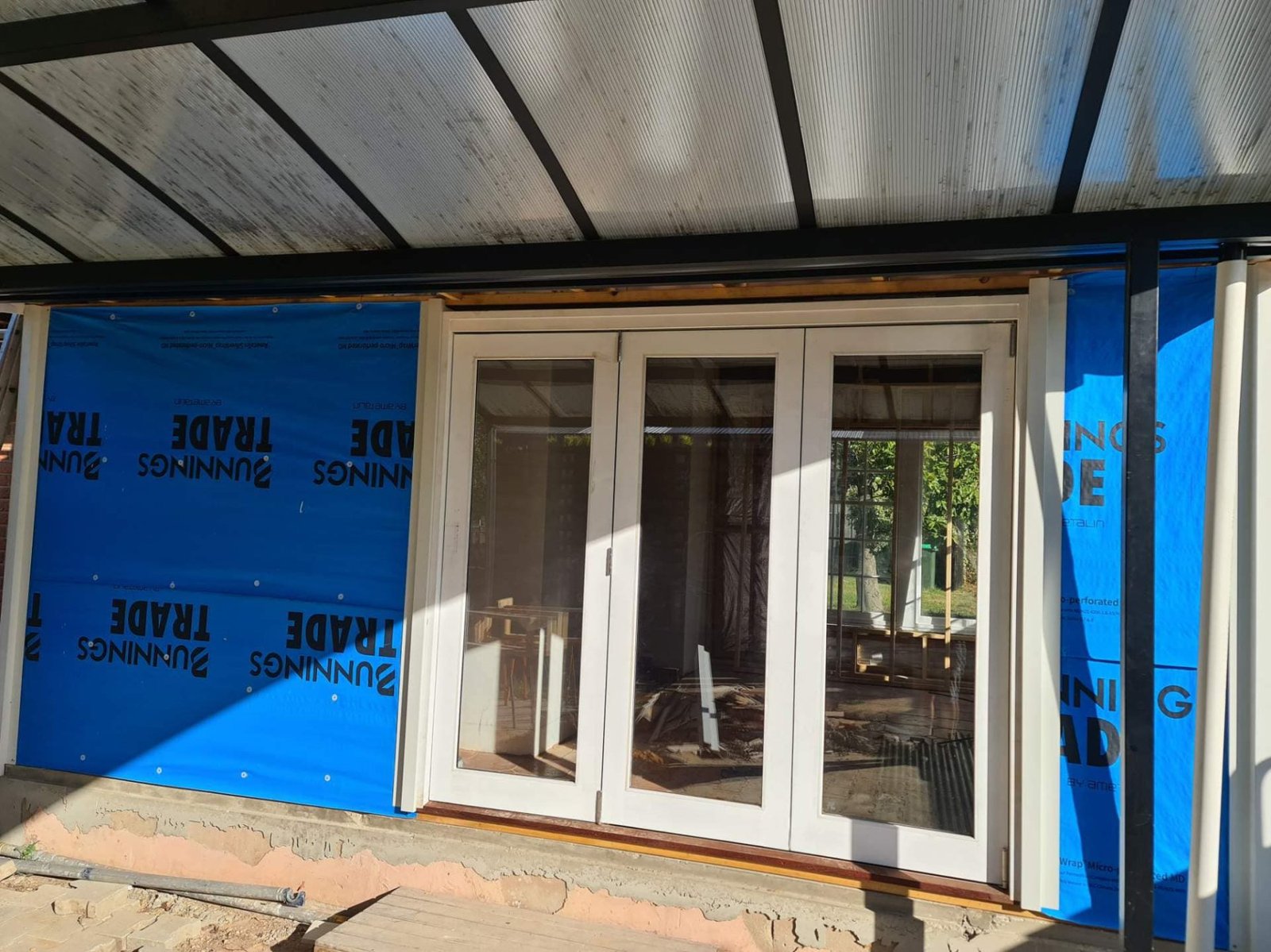 Three-panel white-painted timber bifold door under construction, opening onto a covered patio