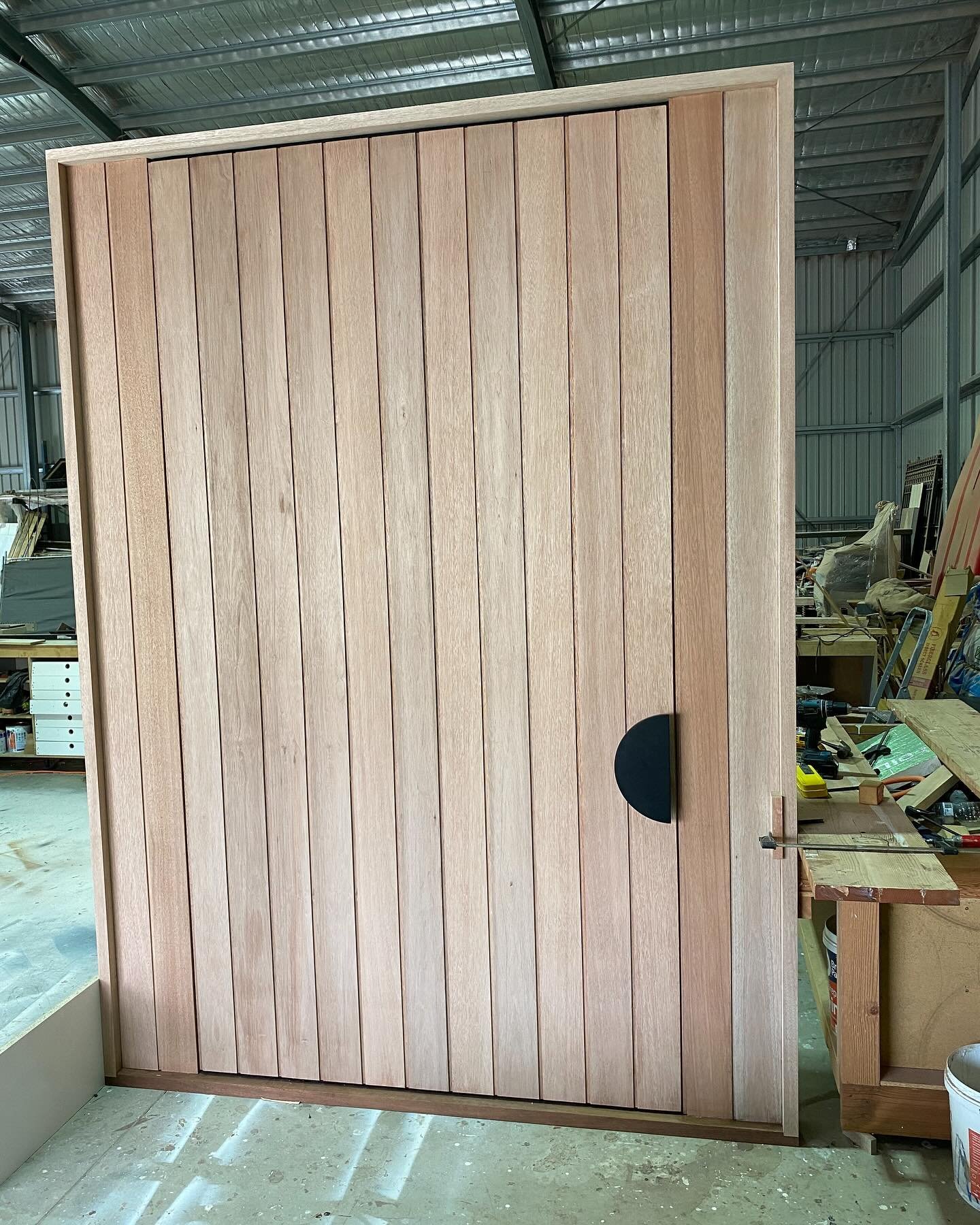 Modern vertical-slat timber entry door with black half-moon handle, finished in the workshop
