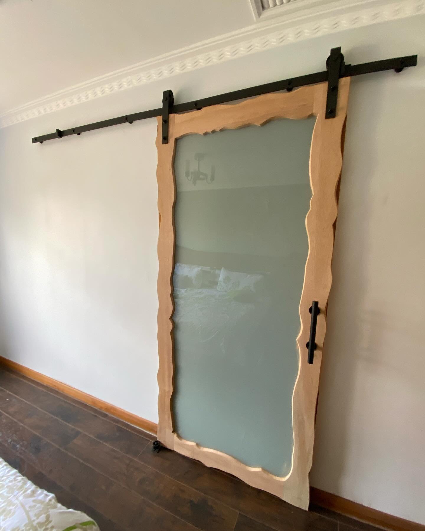 Live-edge timber sliding barn door with frosted glass panel, on black rail track in bedroom