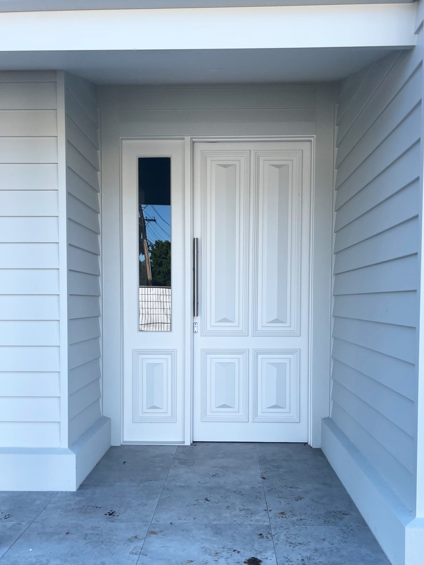 White-painted panelled entry door with a narrow glazed sidelight, under a portico