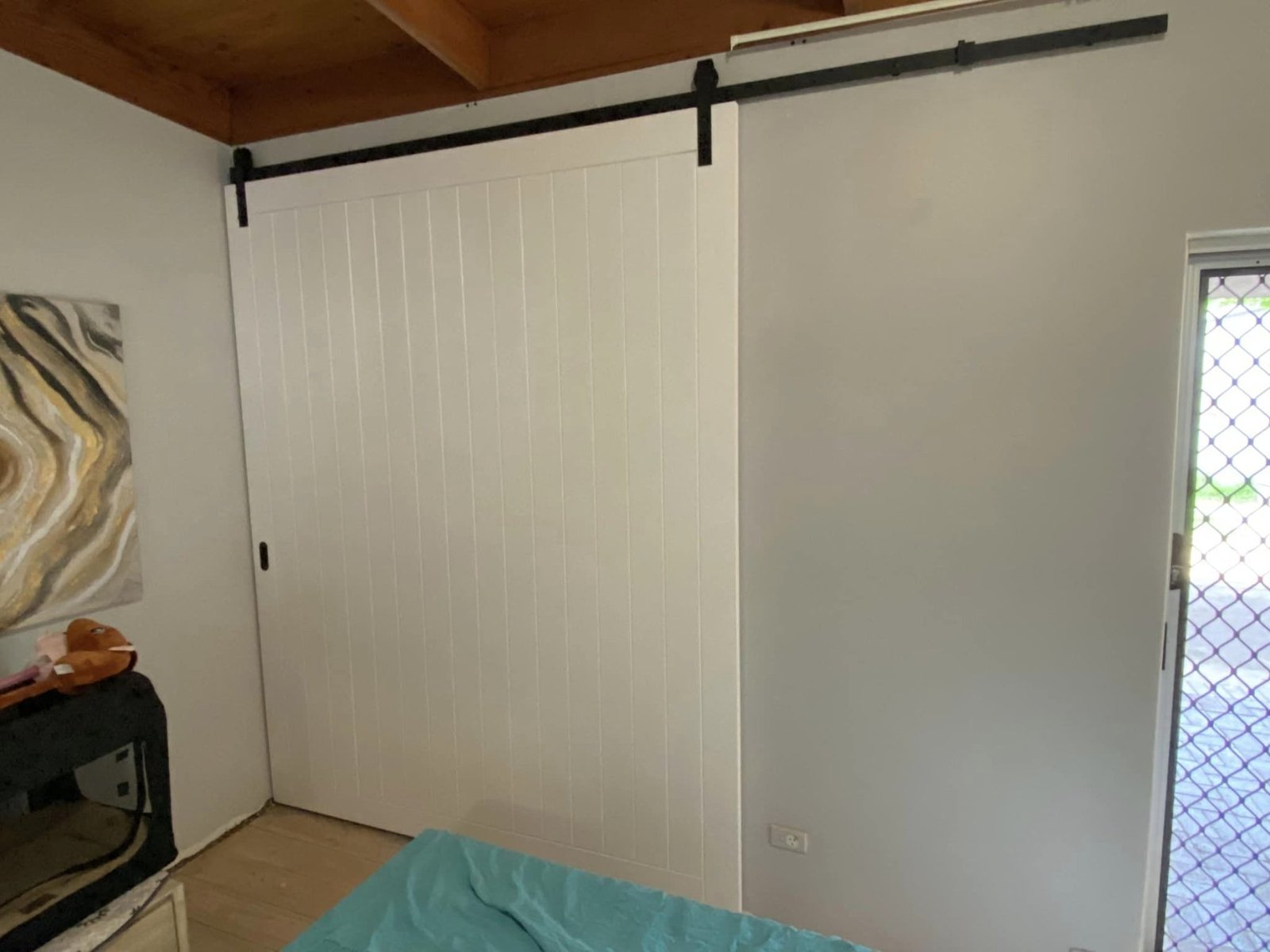 White painted sliding barn door with vertical panelling, on black rail track in bedroom