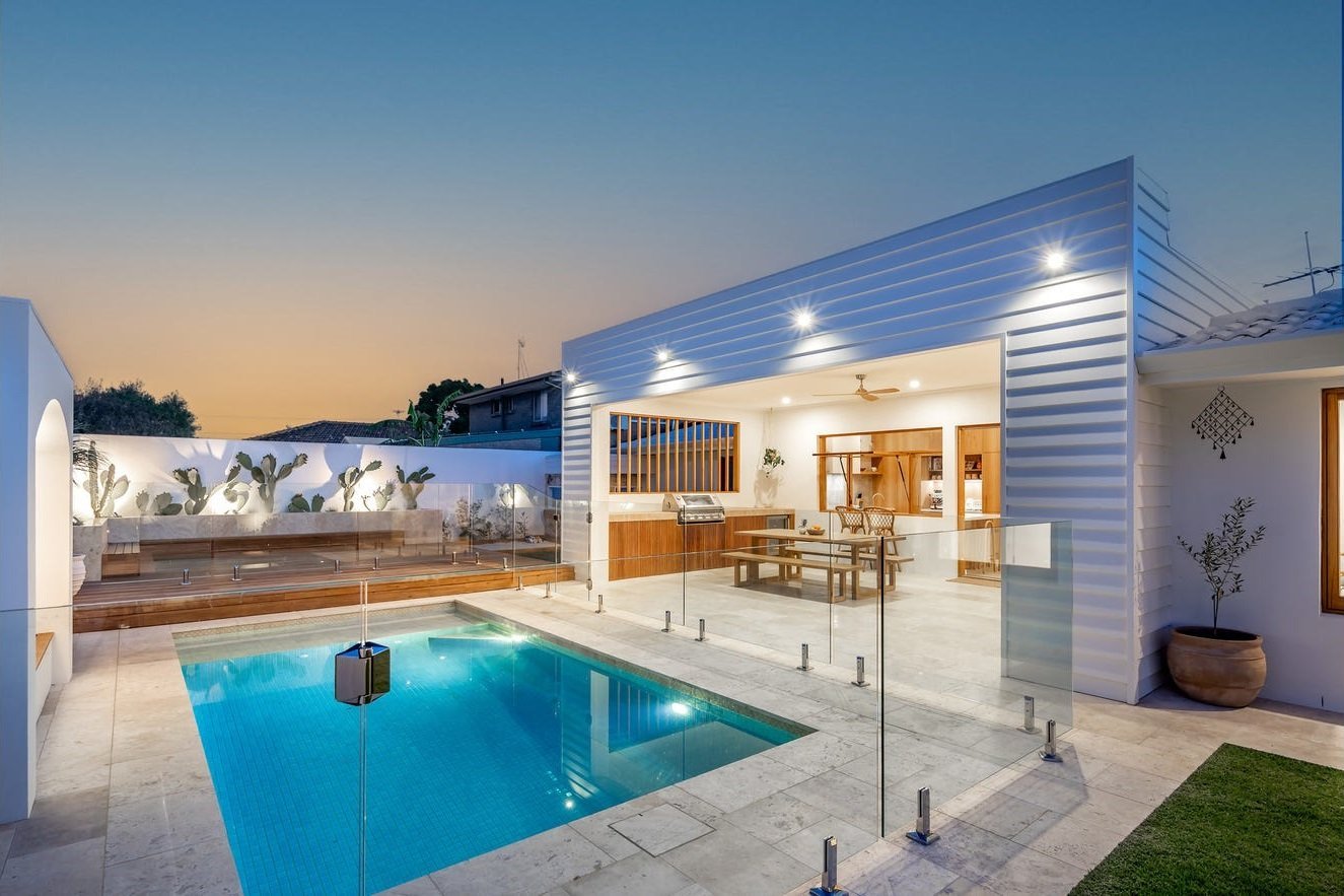 Twilight view of a poolside alfresco pavilion with timber window bank and sliding glass entry