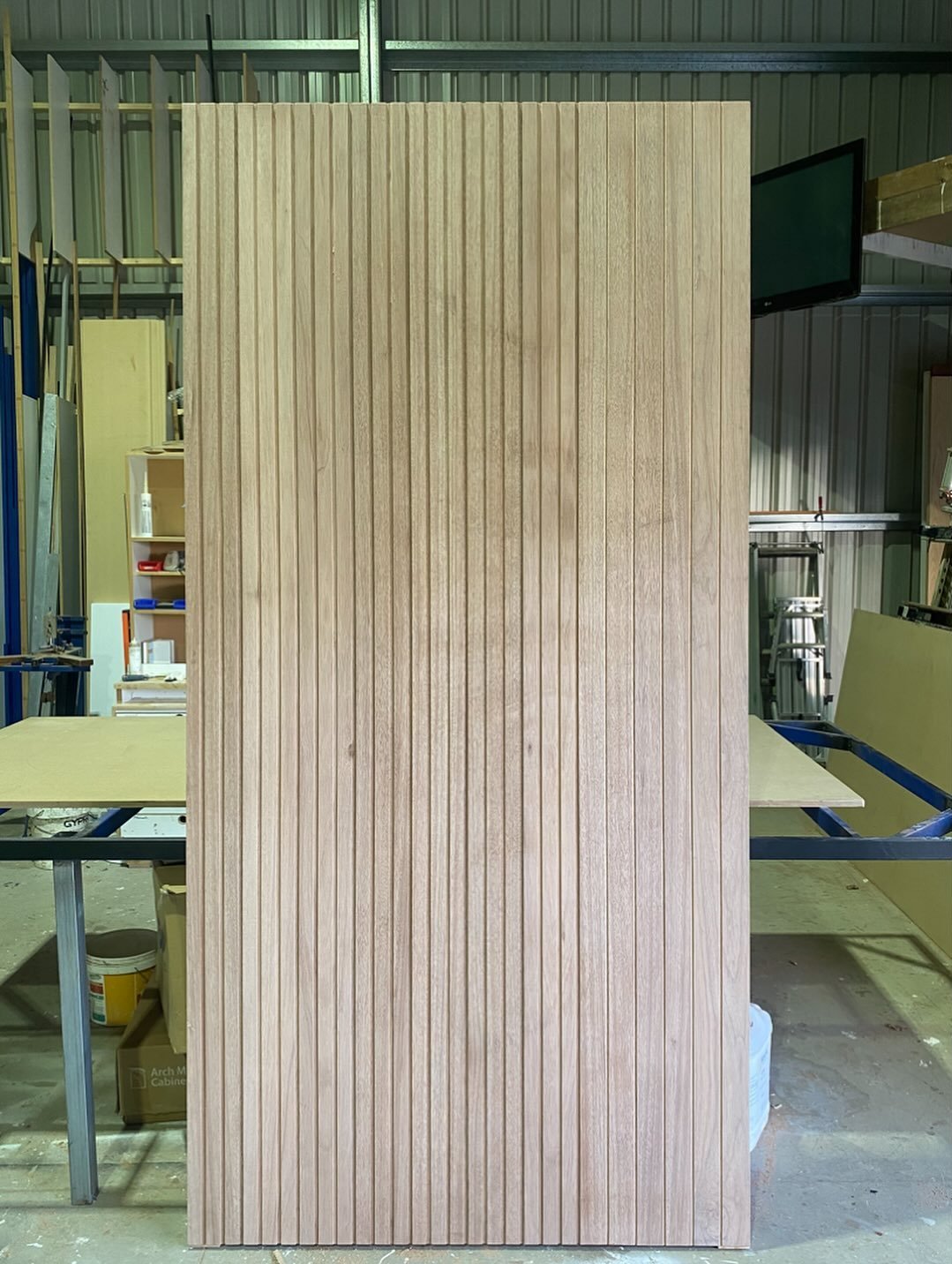 Full-height vertical-slat timber entry door, unstained, standing in the workshop