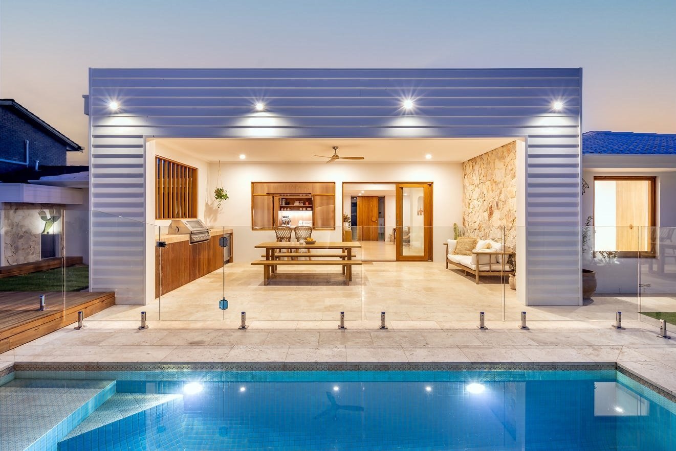 Twilight view of a poolside alfresco room with timber-framed windows and a glazed entry door