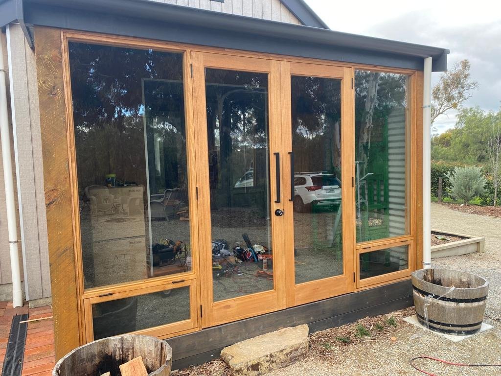Four-panel timber bifold door with glazing, installed on a rustic garden studio